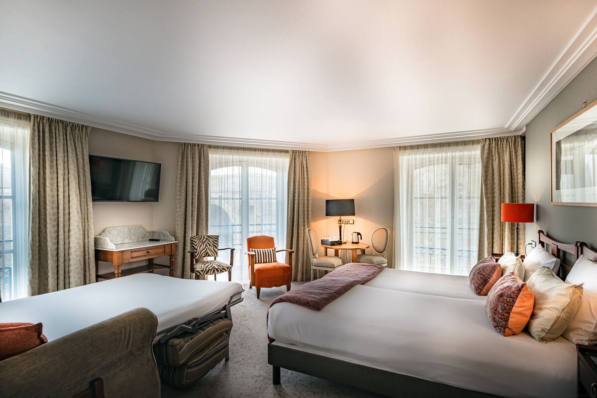 Une chambre d’hôtel avec deux lits, un bureau, une chaise, une télévision et une lampe.