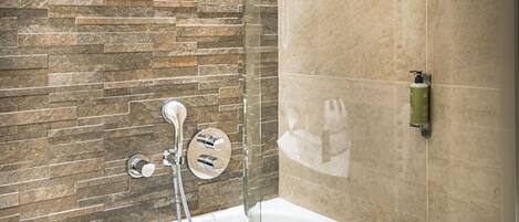 Une salle de bain moderne avec un mur en pierre, une douche à l’italienne et une baignoire blanche.