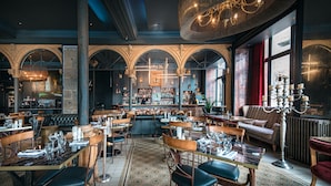 Un restaurante con techos altos abovedados, una zona de bar y un espacio de asientos con mesas y sillas.