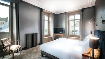 A hotel room with a large bed, a chair, a TV, and a window with curtains.
