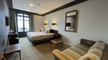 Habitación de hotel con cama, sofá, escritorio y ventana con cortinas.