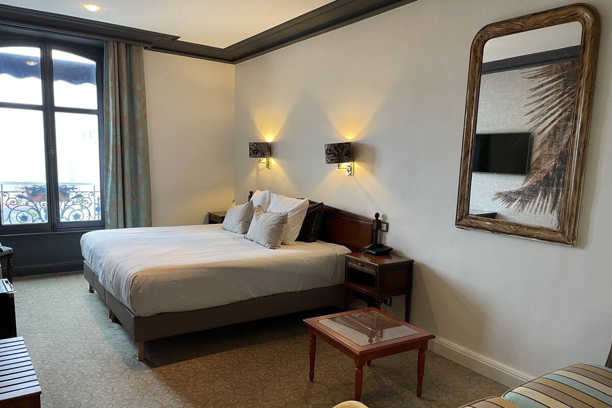 Une chambre d’hôtel avec un grand lit, deux lampes de chevet, une petite table, un canapé et un grand miroir au mur.