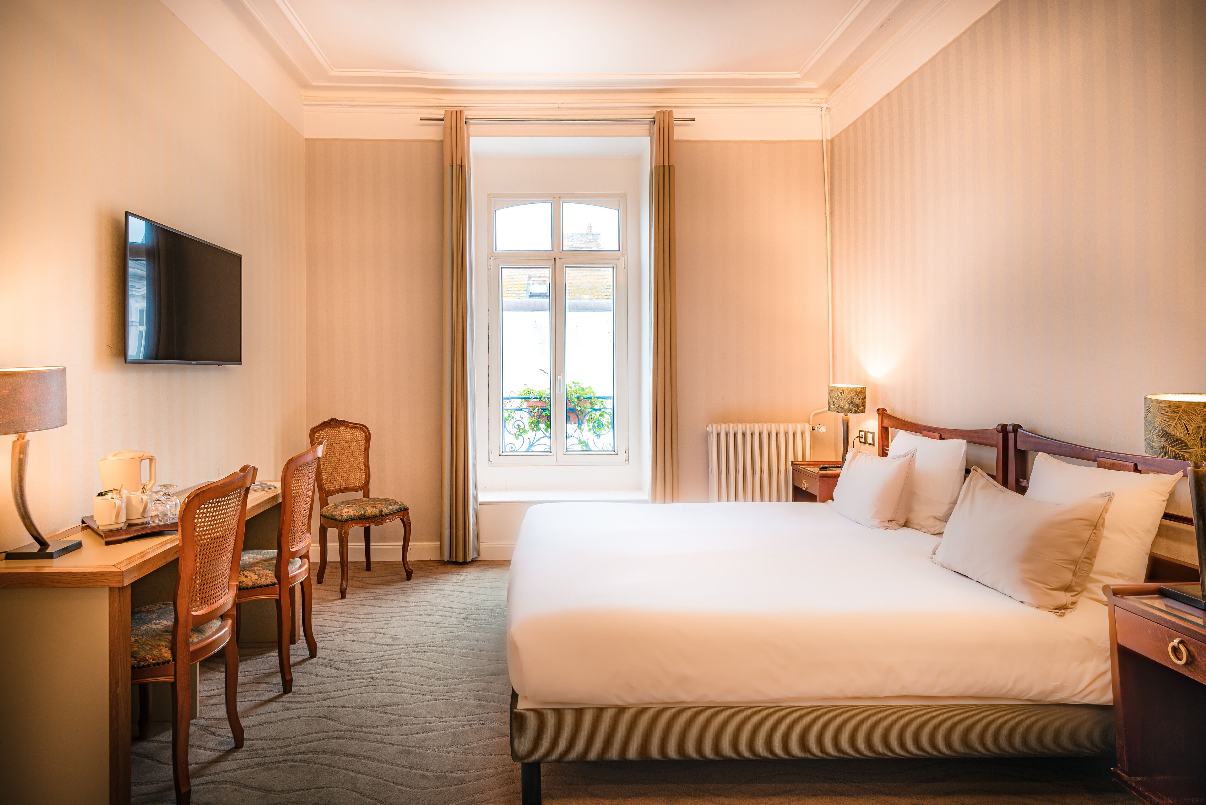 A hotel room with a bed, a desk with a chair, a television, and a window with curtains.