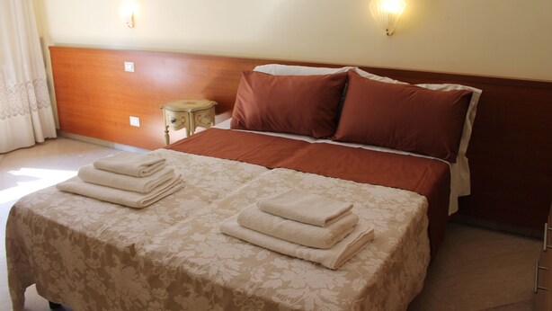 A neatly made bed with a floral bedspread and two pillows, a bedside table with a lamp, and a wooden headboard. - Le Terrazze del Vaticano (Rome)