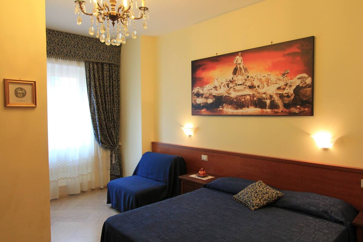 A hotel room with two beds, a chandelier, a painting, and a clock on the wall.