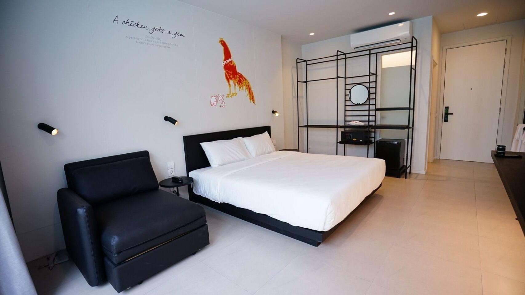 A modern hotel room with a large bed, a black sofa, a desk, and a mirror.