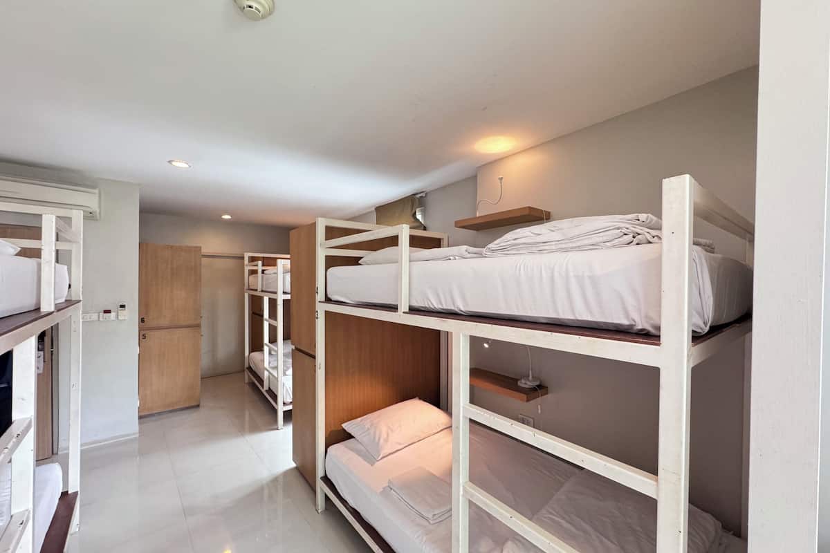 A dormitory-style room with bunk beds, a wooden wardrobe, and a kitchenette area.