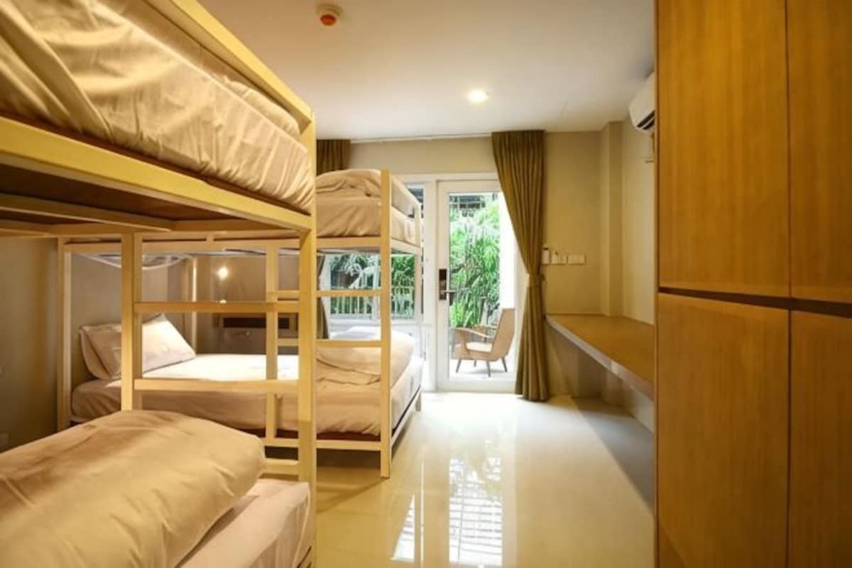 A room with bunk beds, a wooden wardrobe, and a chair near a sliding glass door.