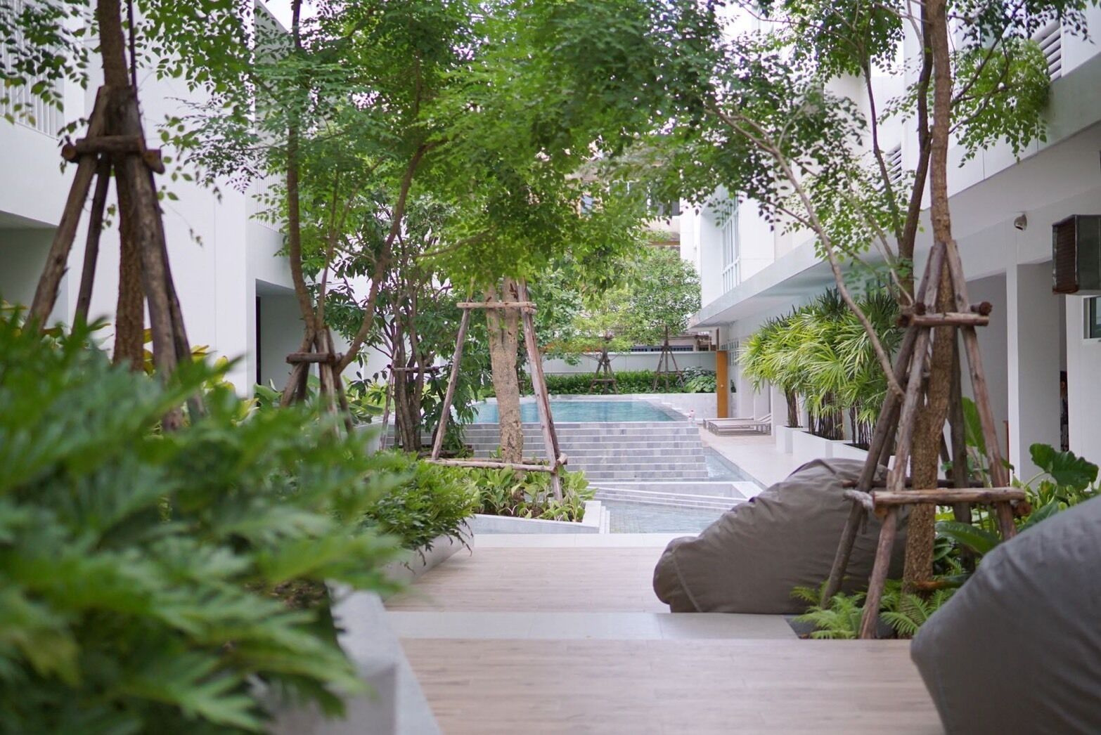 Un jardín interior moderno con piscina, estructuras de madera y plantas en macetas.