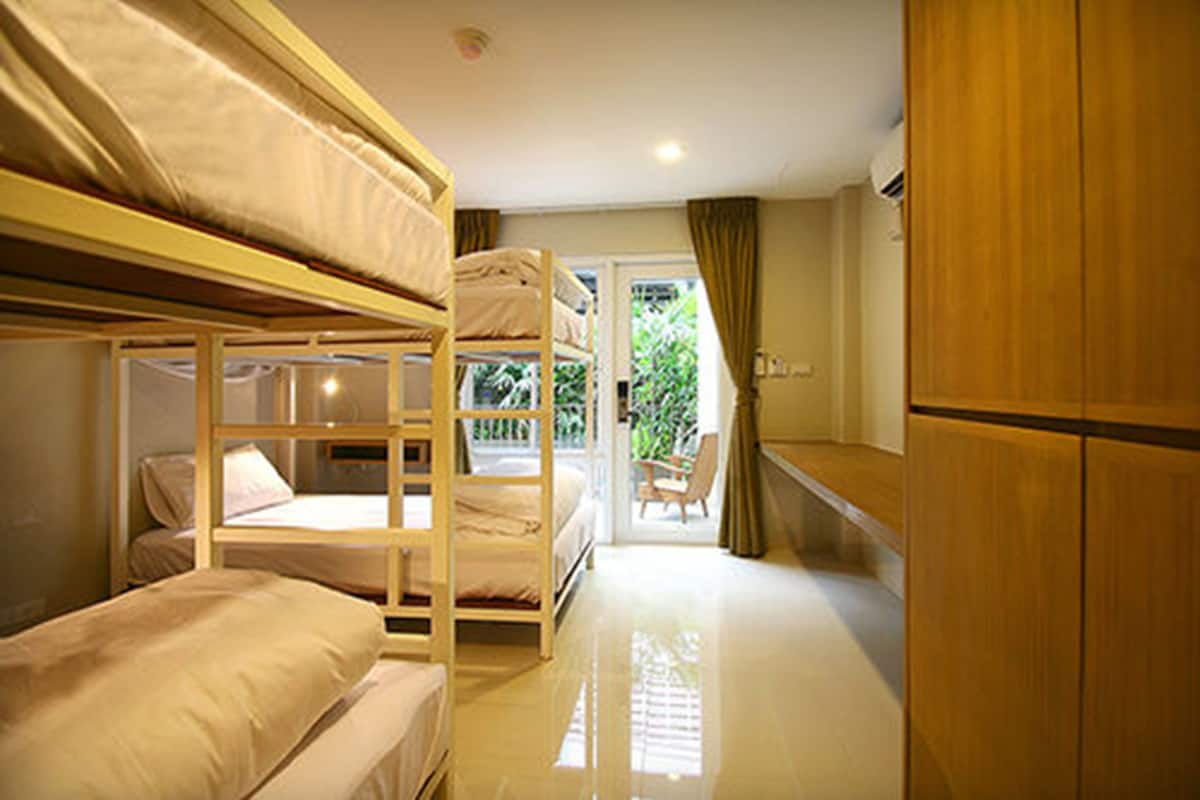 A bunk bed room with a wooden desk and a chair, a small table, and a door leading to a balcony.