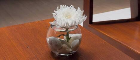 Ein Holztisch mit einer klaren Glasvase, gefüllt mit weißen Blumen und glatten Steinen.