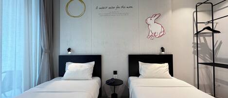 A hotel room with two beds, a wall-mounted artwork of a rabbit, and a small table with a lamp.