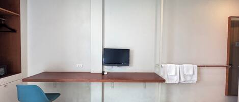 Una habitación moderna y minimalista con un escritorio de madera, una silla azul, un televisor de pantalla plana montado en la pared y un perchero.