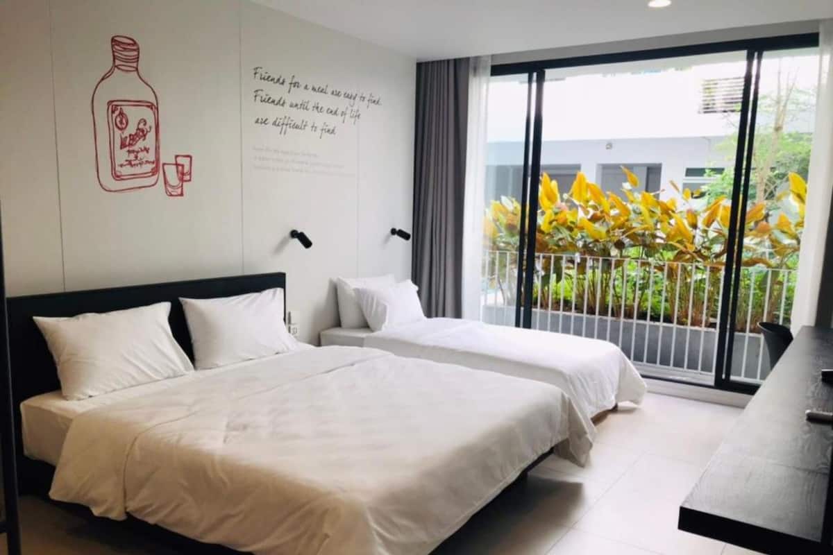 A hotel room with two beds, a large window with a view of yellow foliage, and a wall with a quote and a drawing of a bottle.