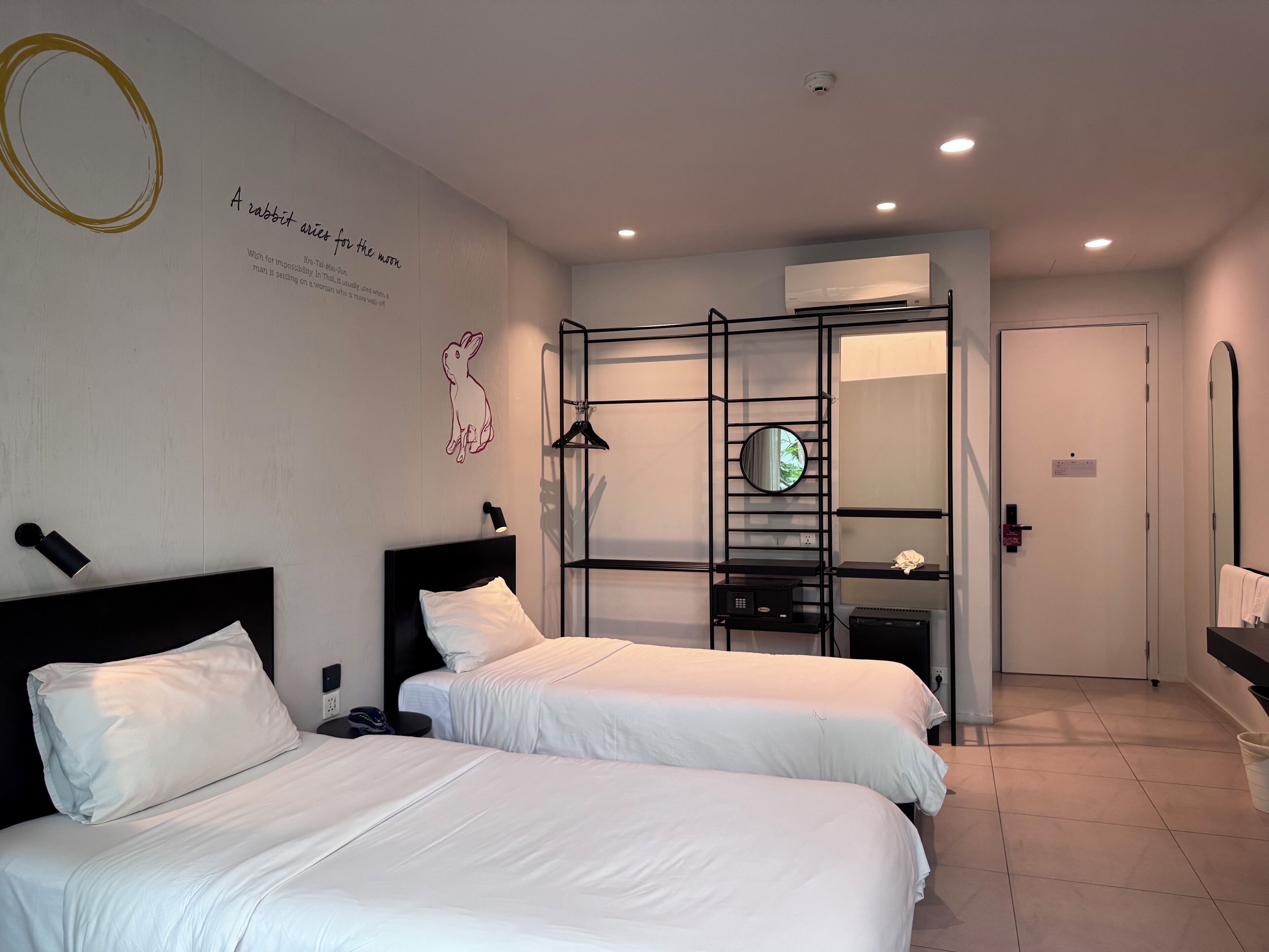 A hotel room with two beds, a wardrobe, a mirror, and a wall with a rabbit illustration.