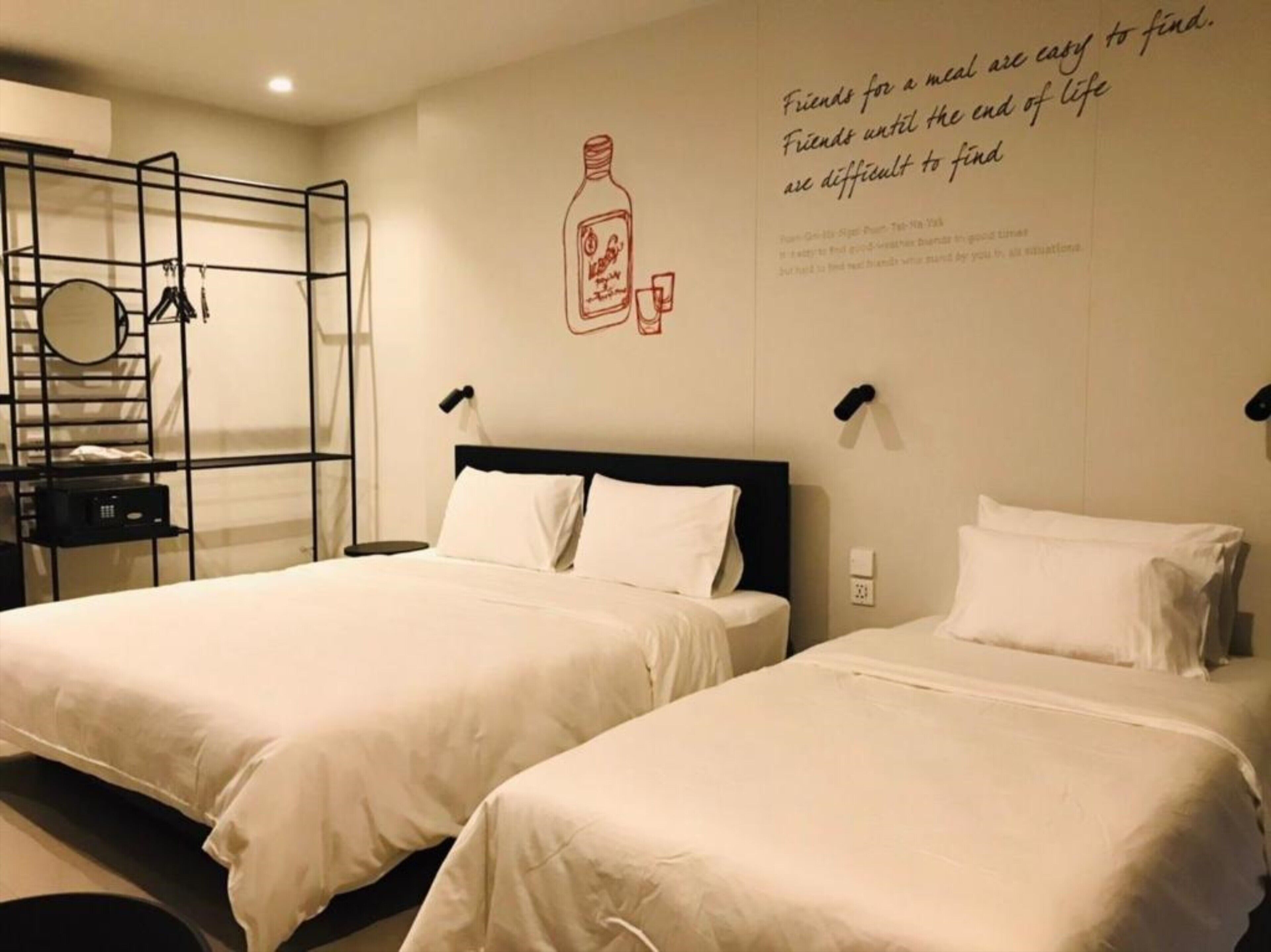 A hotel room with two beds, a wall-mounted shelf, a mirror, and a decorative wall with a quote.