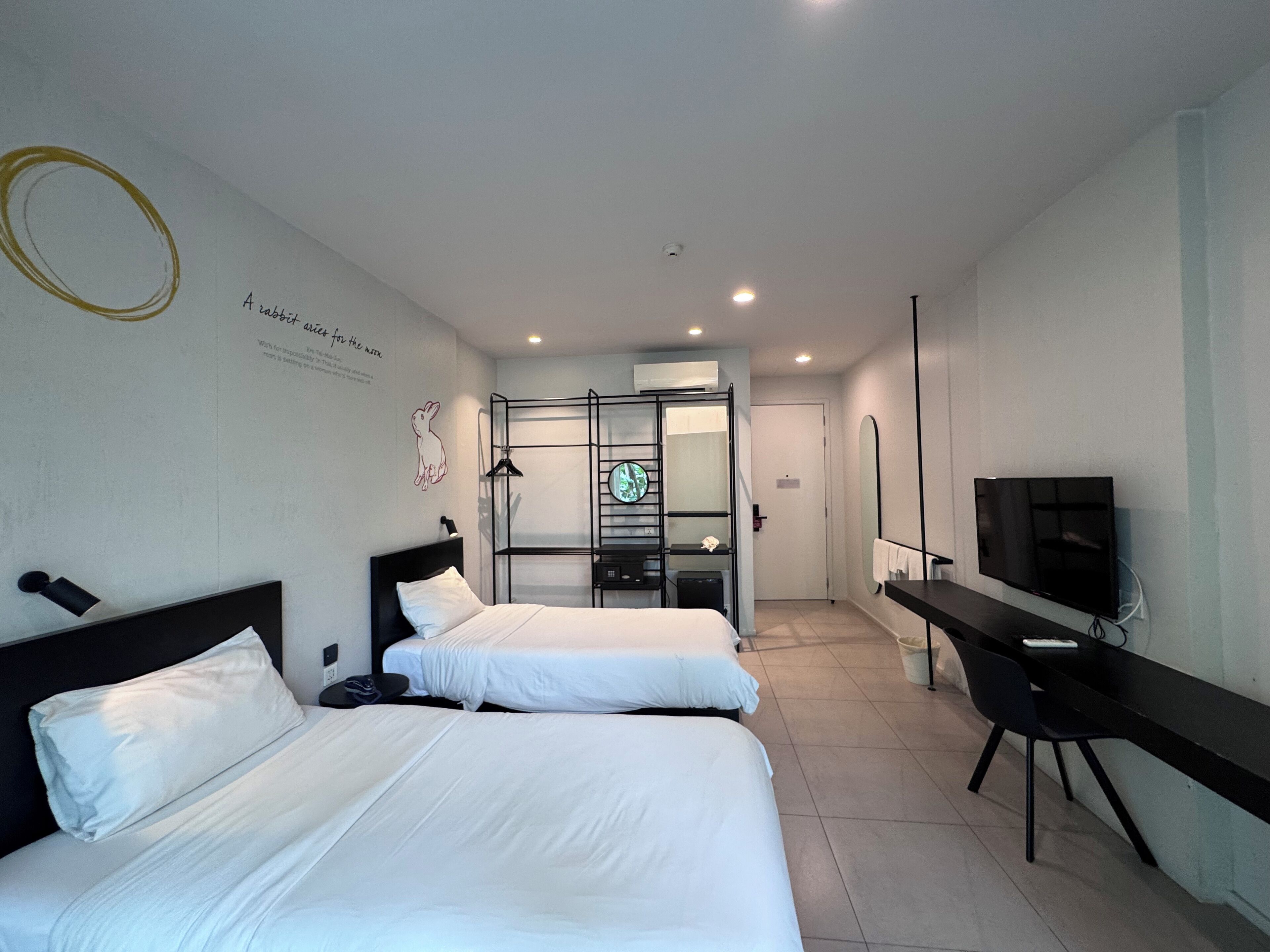 Une chambre d’hôtel avec deux lits, un bureau, une télévision et une salle de bain visible à travers une porte en verre.