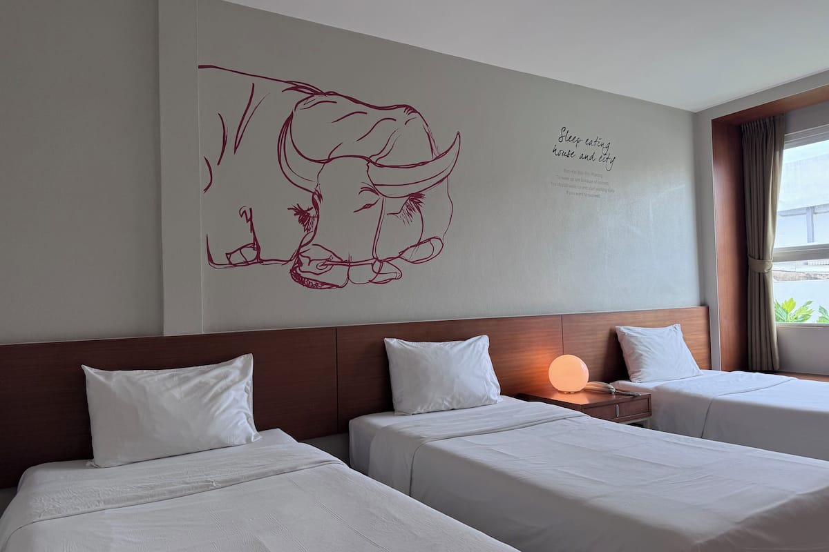 A hotel room with two beds, a wall mural, and a window with curtains.