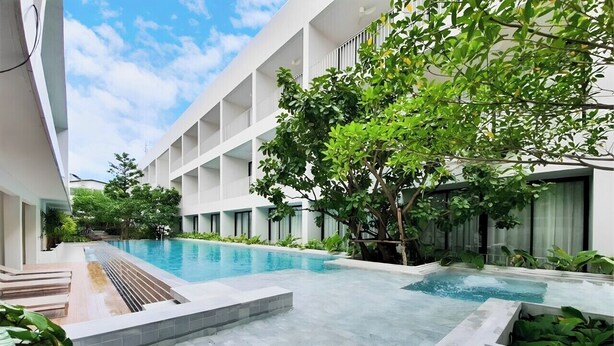Ein moderner Hotelinnenhof mit einem Schwimmbad, umgeben von üppiger Bepflanzung und einem mehrstöckigen Gebäude.