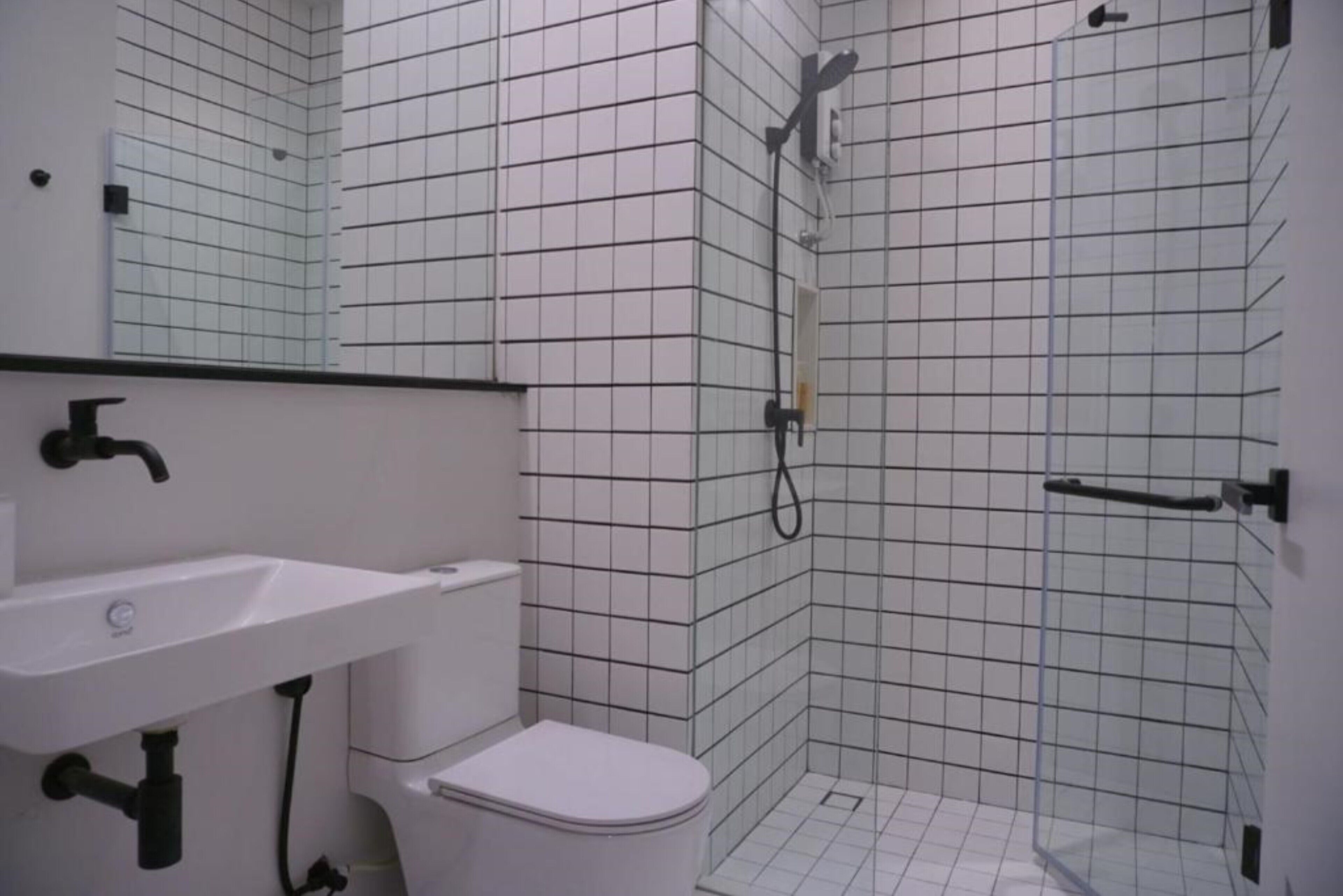 Une salle de bain avec un lavabo blanc, des toilettes et un espace douche dont les murs et le sol sont recouverts de carrelage.