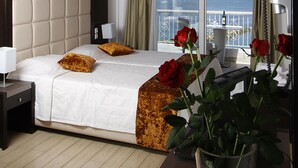 A bedroom with a large bed, wooden ceiling beams, a view of the sea, and a vase with red roses.