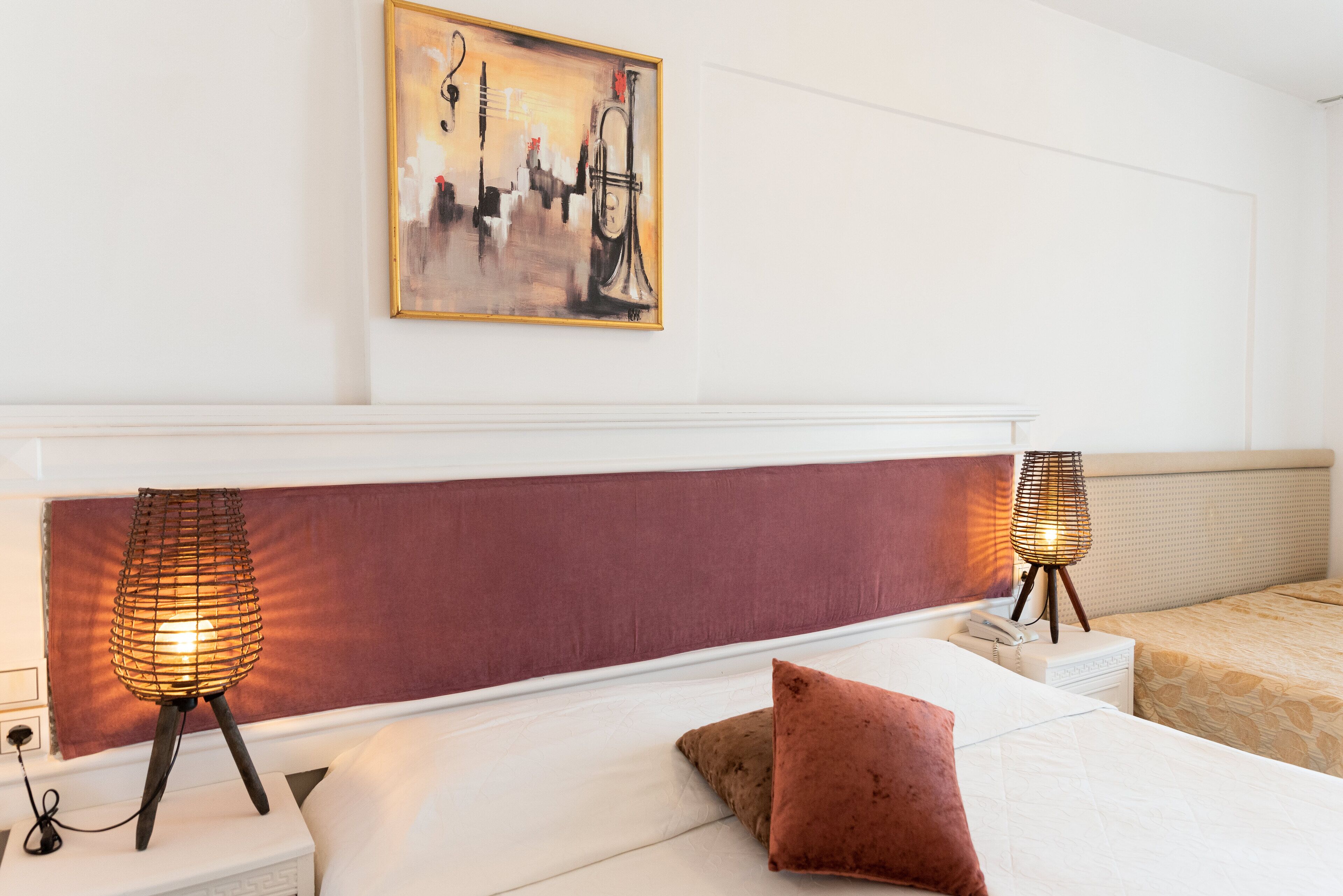 Una habitación de hotel con una cama grande, dos lámparas de noche, un cuadro en la pared y un cabecero con un panel rojo.