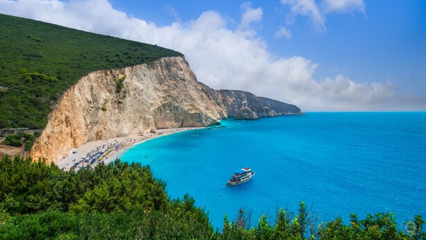 A coastal landscape with a cliff, beach, and clear blue sea.