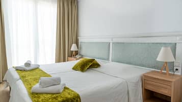 A hotel room with two beds, a nightstand with a lamp, a window with curtains, and a wall with a patterned design.
