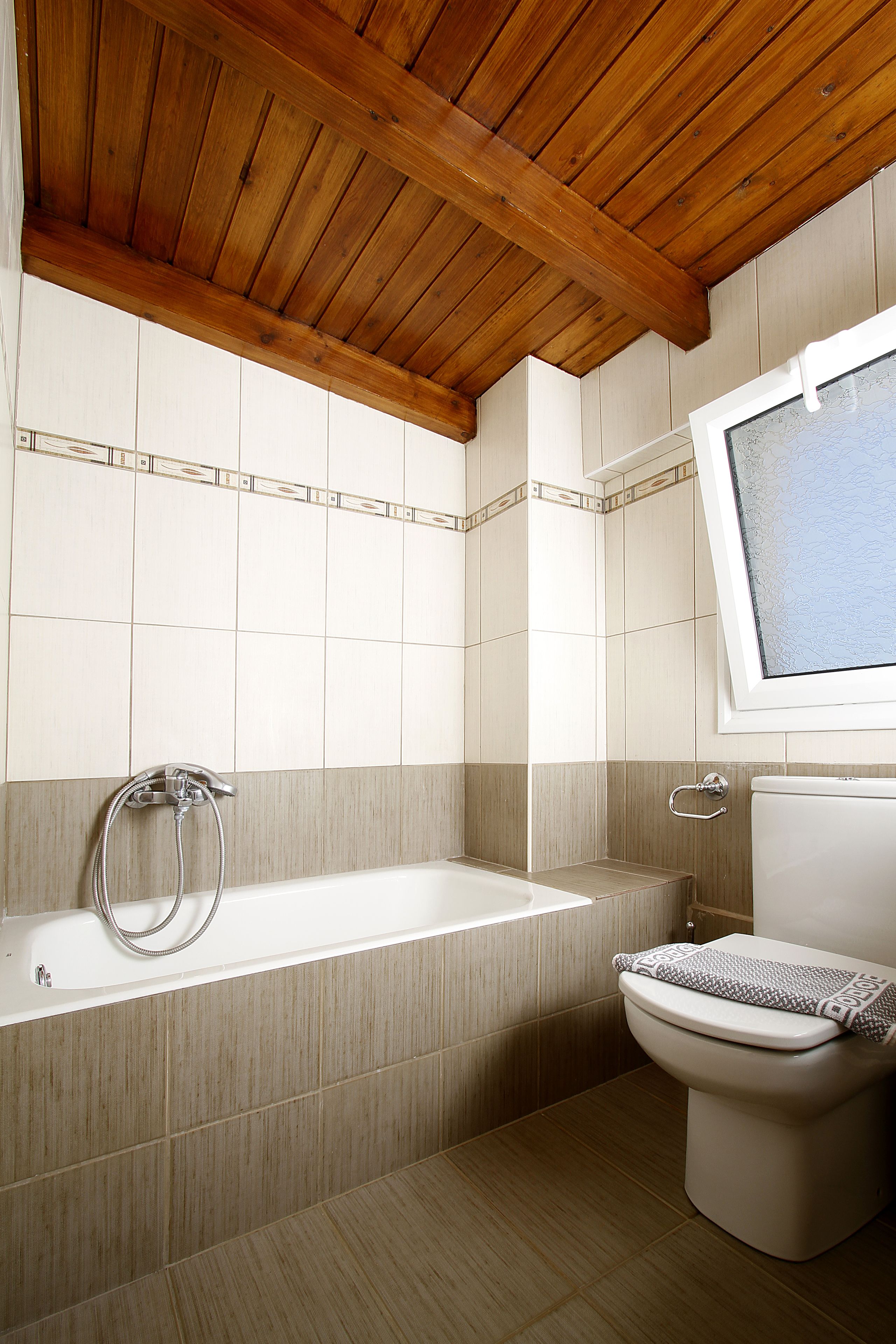 Un baño con techo de madera, una bañera, un inodoro y una ventana.