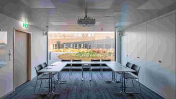 A conference room with a long table, chairs, a projector, and a view of a garden through large windows.