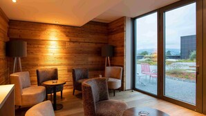 A modern lounge with wooden walls, comfortable seating, and large windows offering a view of the outdoors. - HOTEL illuster - Urban & Local (Uster)