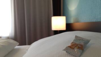 A hotel room with a neatly made bed, a pillow, and a packet of snacks on the bed.