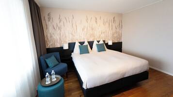 A hotel room with a large bed, a bedside table with water bottles, a blue armchair, and a wall with a nature-themed mural.
