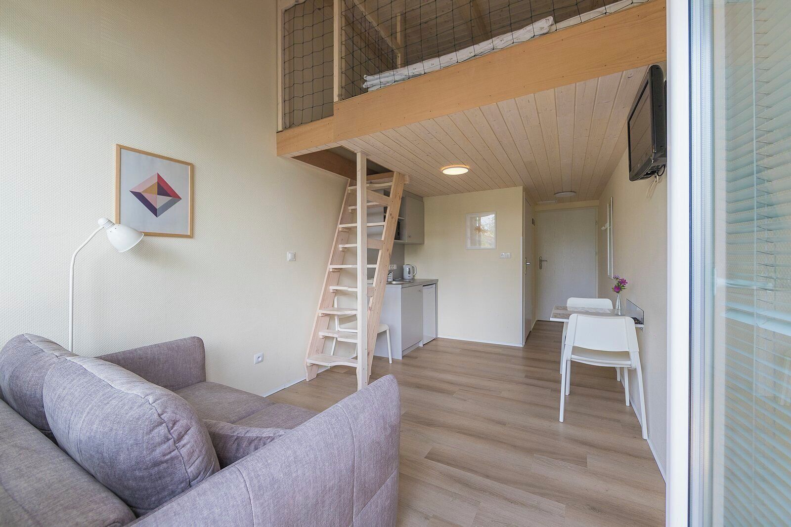 Ein Loft-Zimmer mit Holzleiter, einer Couch, einem Schreibtisch und einem Fernseher.
