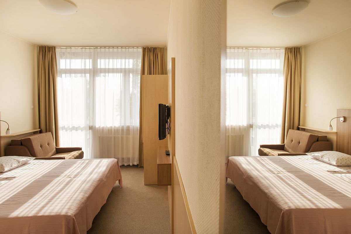 A hotel room with two beds, a wardrobe, a TV, and a desk.