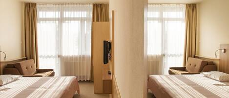 A hotel room with two beds, a wardrobe, a TV, and a desk.
