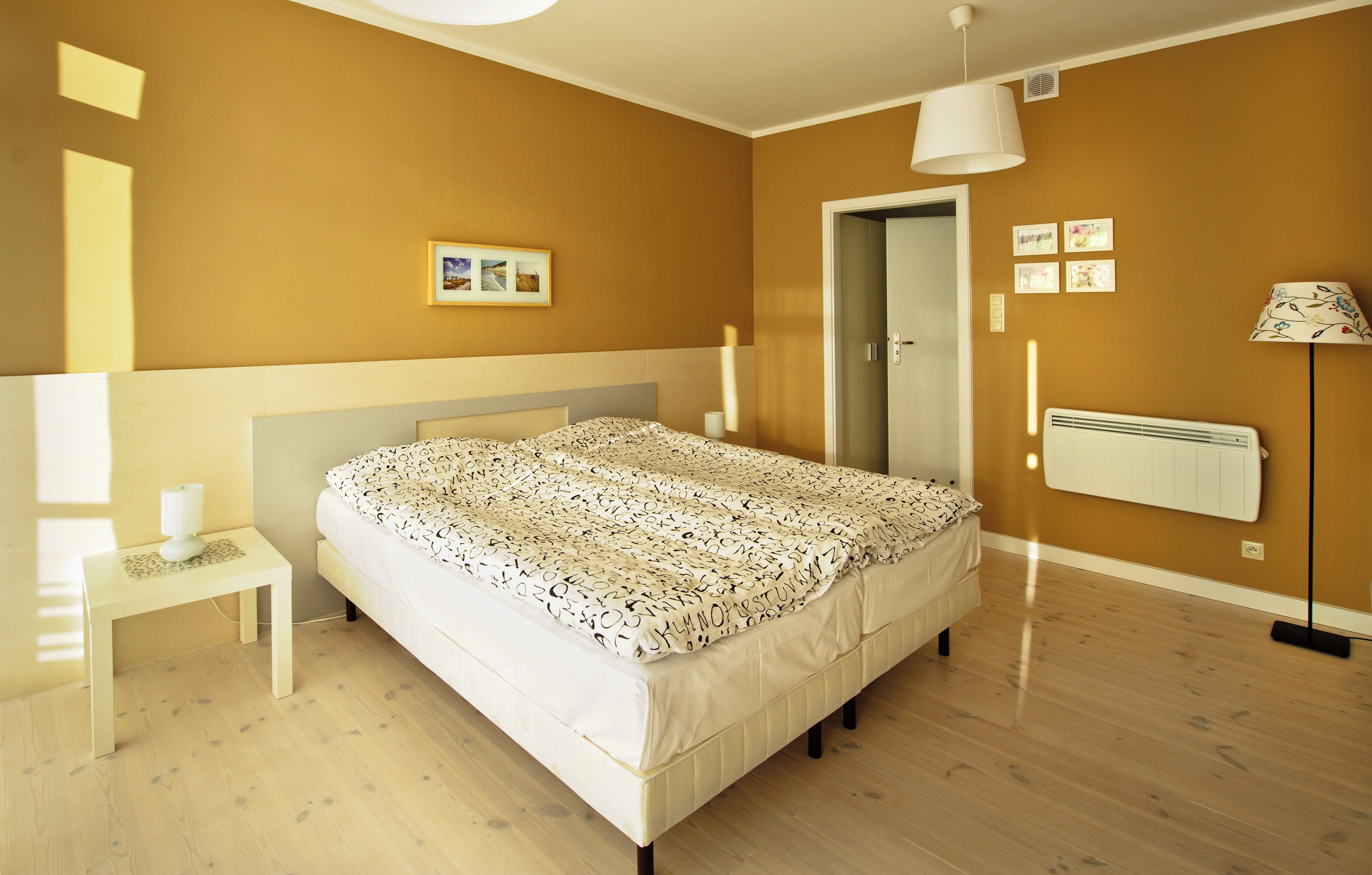 A bedroom with a bed, bedside table, lamp, radiator, and wall-mounted pictures.