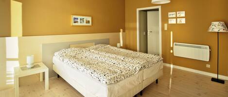 A bedroom with a bed, bedside table, lamp, radiator, and wall-mounted pictures.