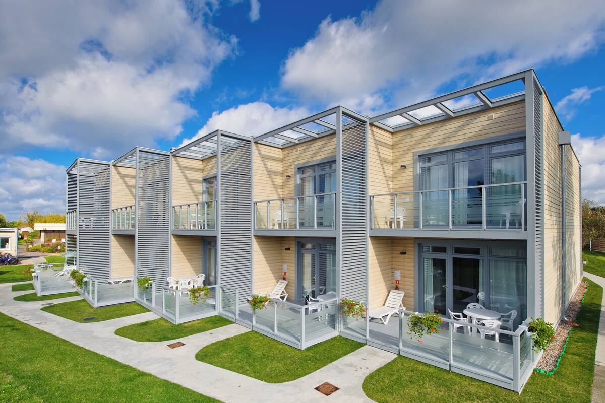 Un hotel moderno de varios pisos con balcones de vidrio, mobiliario exterior y un césped bien cuidado.