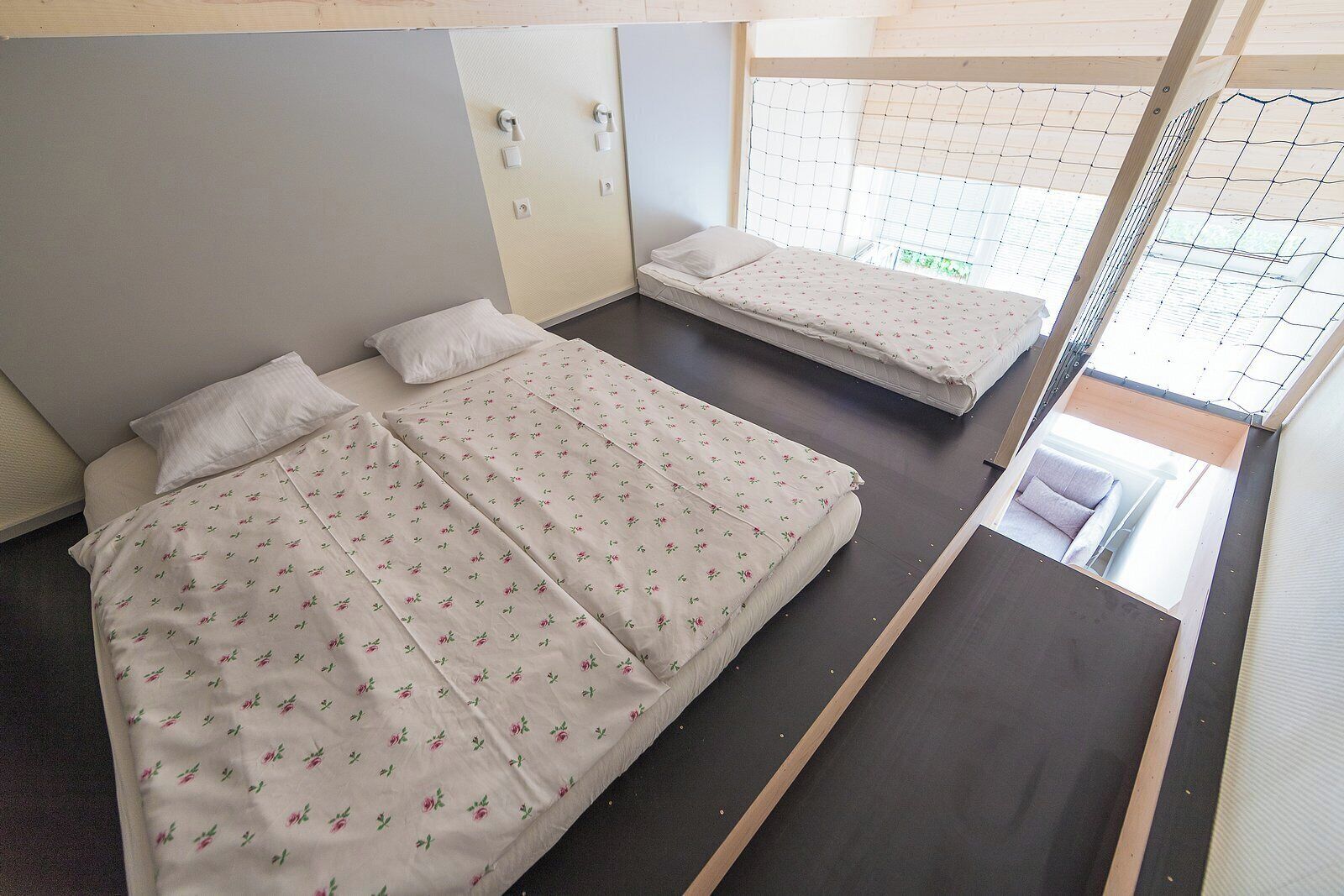 A room with two beds, each with a floral-patterned bedspread, a small window with a view, and a wooden ceiling.