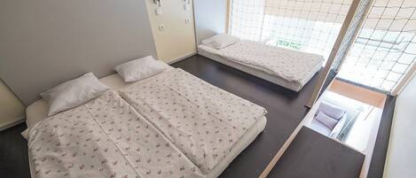 A room with two beds, each with a floral-patterned bedspread, a small window with a view, and a wooden ceiling.