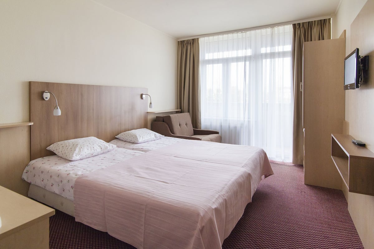Habitación de hotel con una cama grande, un escritorio, una silla, un televisor y una ventana con cortinas.