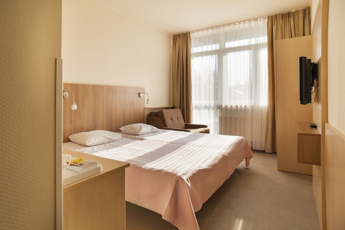 Habitación de hotel con cama, mesita de noche, lámpara, silla y televisor montado en la pared.