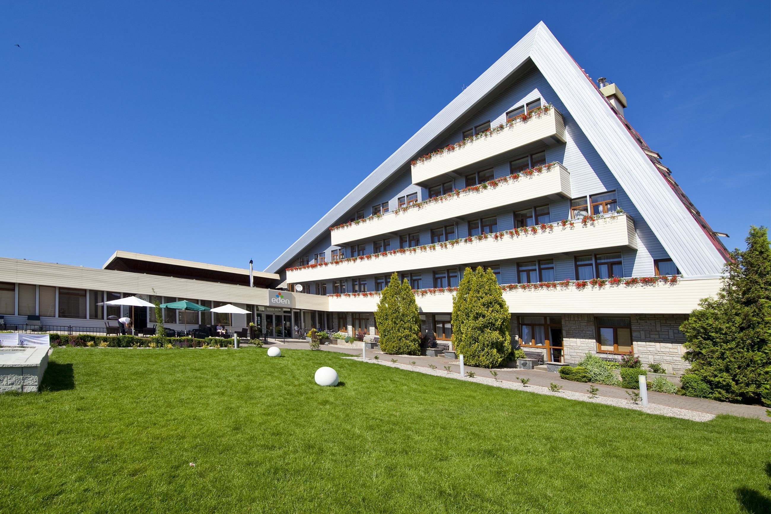 A modern building with a sloped roof, multiple balconies with flower boxes, and a well-maintained lawn with spherical sculptures.