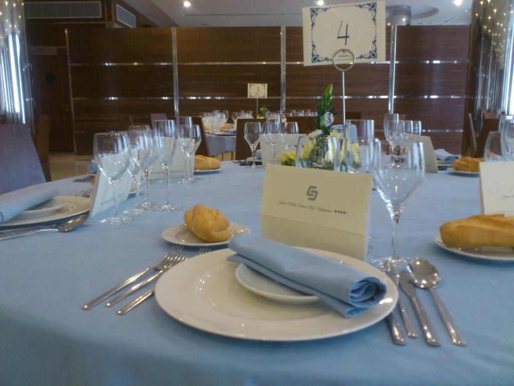 Una mesa de comedor dispuesta con platos, cubiertos y una servilleta doblada, con un cartel de número de mesa y un atril para el menú.