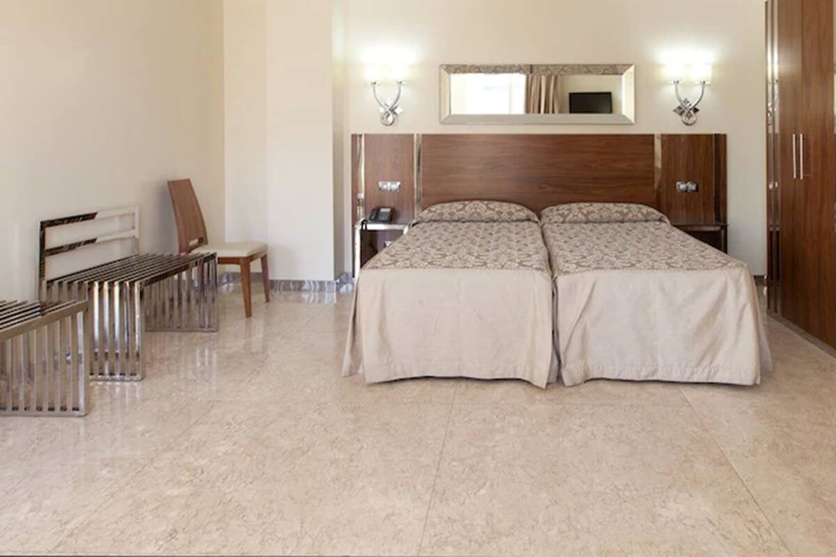 Une chambre d’hôtel avec un lit double, une armoire en bois, un bureau avec une chaise et un banc.