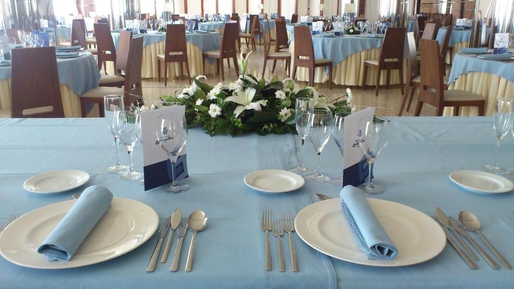 Un salón de banquetes con mesas dispuestas para un evento formal, con manteles azules, platos blancos y cubertería.