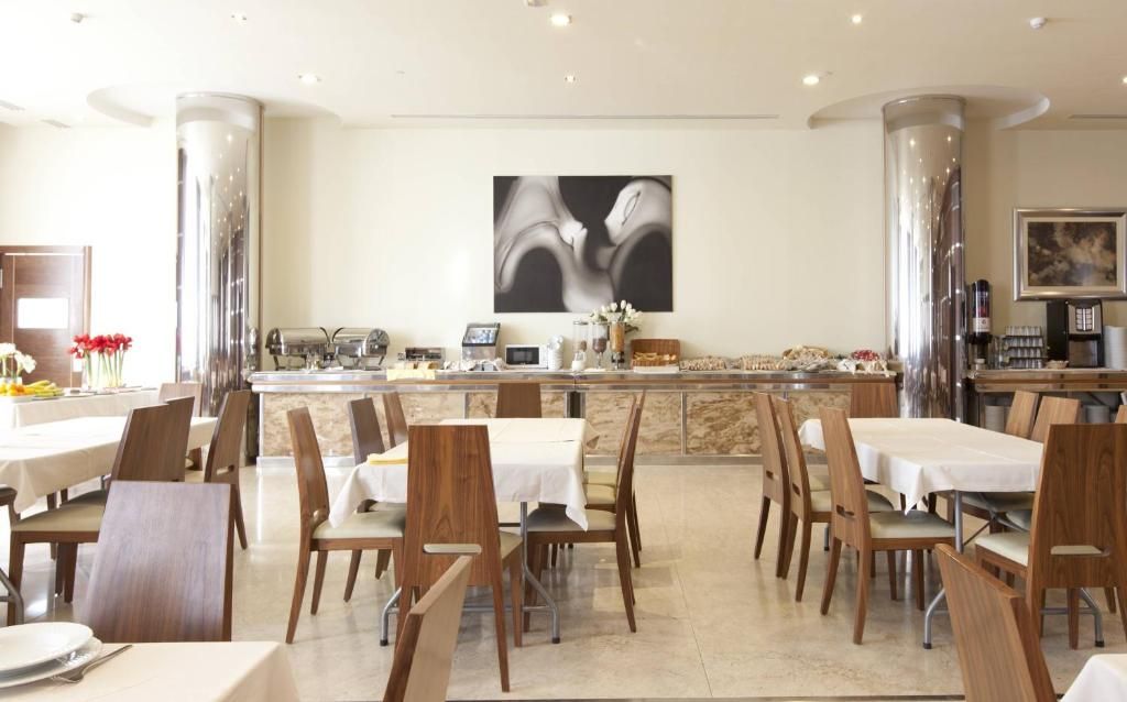 Un comedor con varias mesas y sillas, una barra central y un gran cuadro abstracto en la pared.