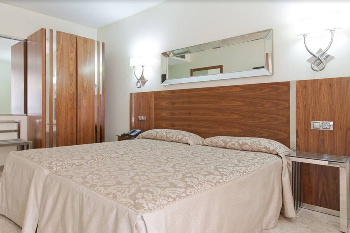 Une chambre avec un grand lit, une armoire en bois, une table de chevet et un miroir.