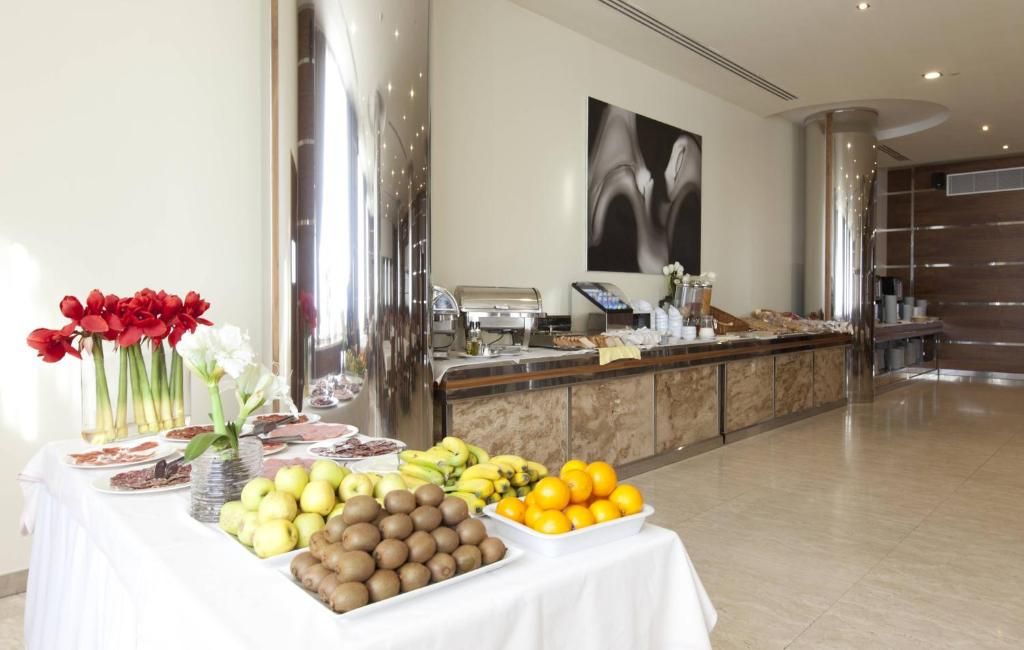 Zona de buffet con diversas frutas y verduras, estación de café y una amplia obra de arte abstracta en la pared.